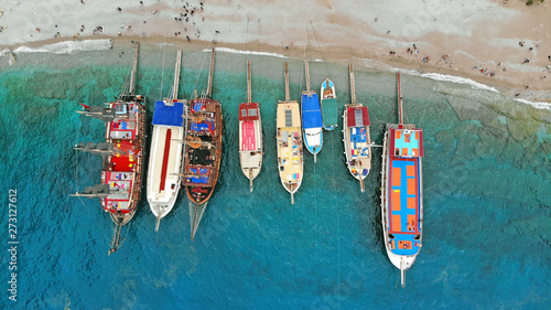 Boats in the sea, top view. Aerial view of colorful boats standing abreast on the shores of the Mediterranean sea in azure water. Tourists crowd are on the beach. Nautical background and summer travel