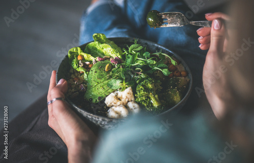 Healthy dinner or lunch at home. Vegan superbowl or Buddha bowl with hummus, vegetable, fresh salad, beans, couscous and avocado in female hands photo