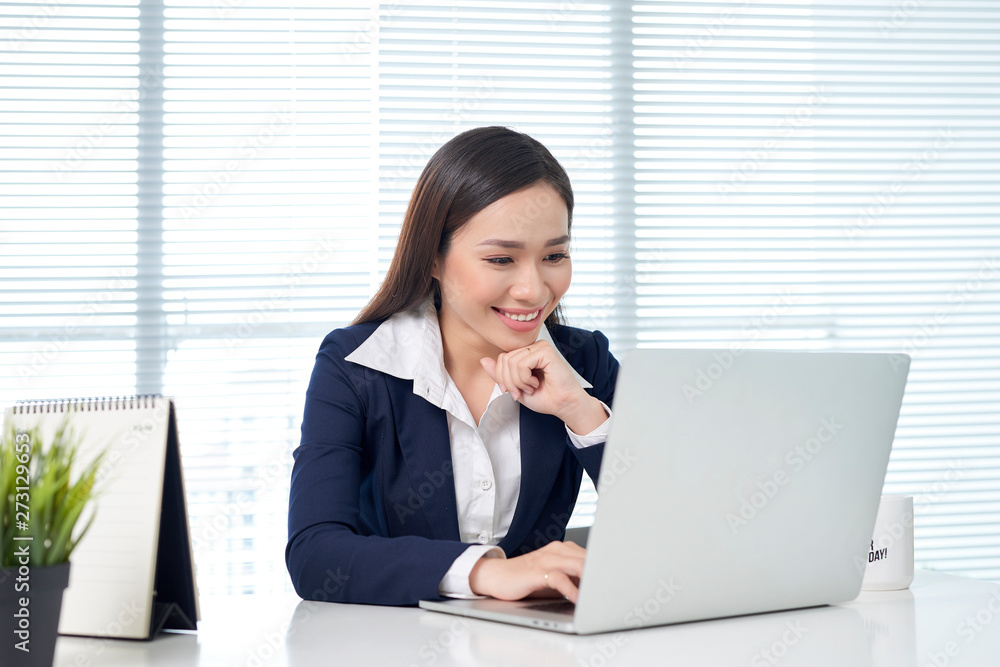 Cheerful employee is holding glasses and looking at screen of laptop with bright smile Cheerful employee is holding glasses and looking at screen of laptop with bright smile