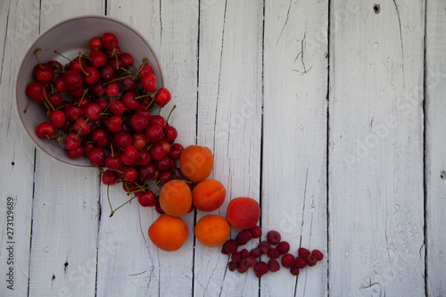 scattered berries from a plate of raspberry cherries apricots on a wooden table