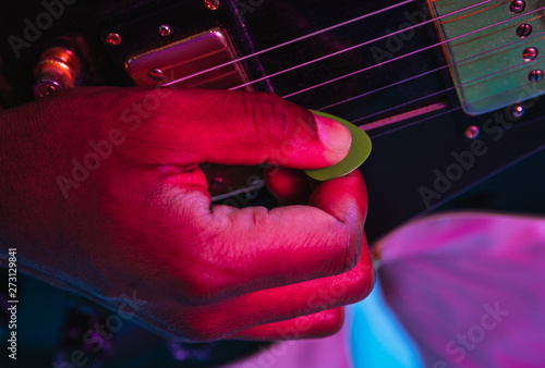 Young african-american musician playing the guitar like a rockstar on blue studio background in neon light. Concept of music  hobby. Joyful attractive guy improvising. Retro colorful portrait.