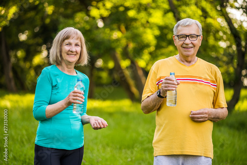 Happy senior couple is drinking water after exercising in park.
