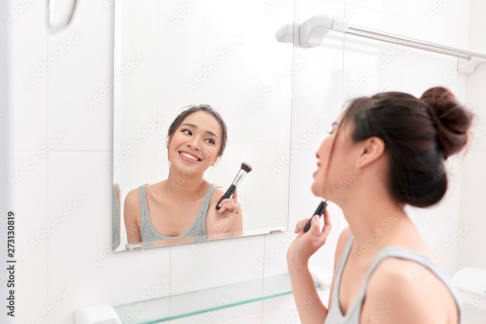 A young woman is standing in front of the bathroom mirror and putting on makeup. A young woman is standing in front of the bathroom mirror and putting on makeup.