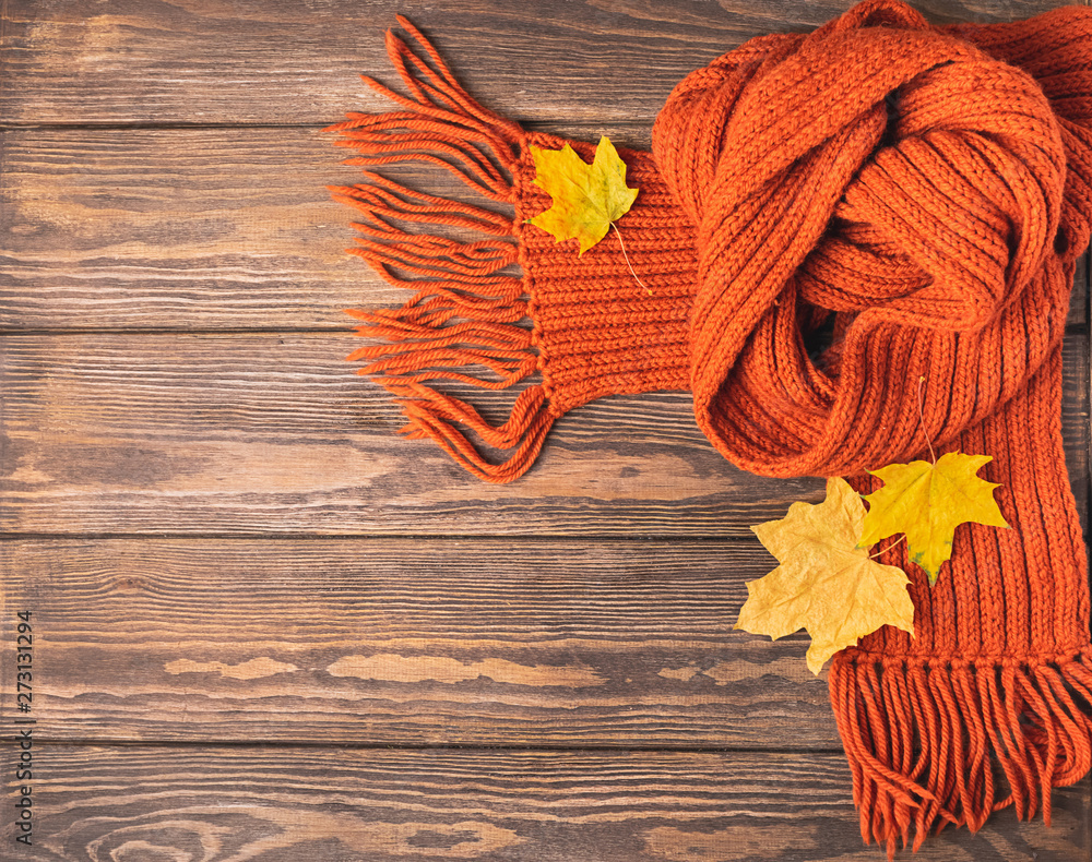 A bright knitted orange knitted scarf and maple leaf lies on a wooden background. Horizontal frame. Autumn concept
