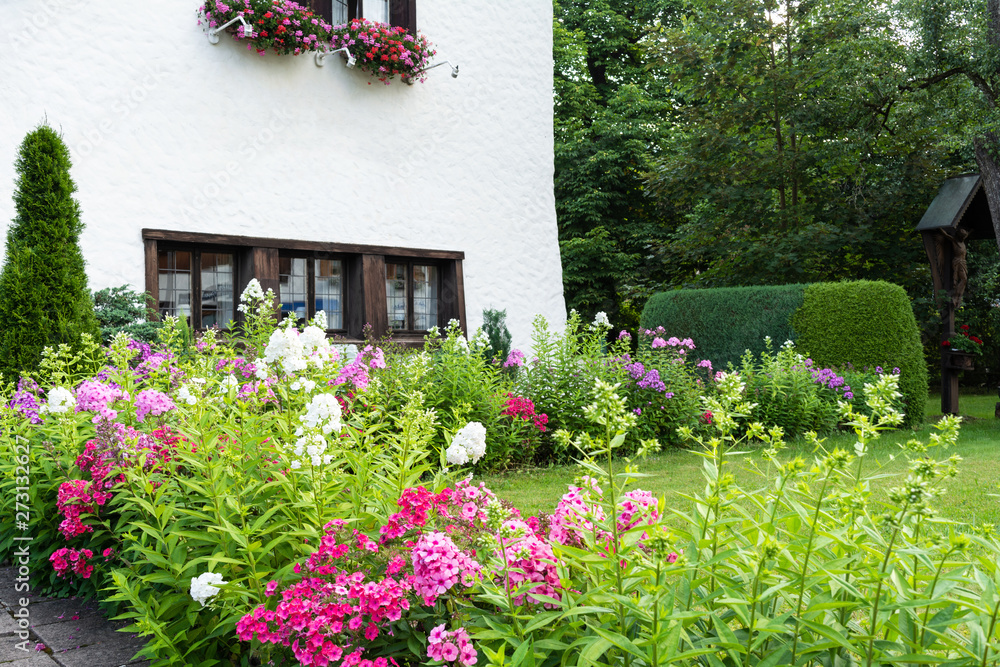 View of the well-kept garden with a green lawn, flowers and trees near the house.