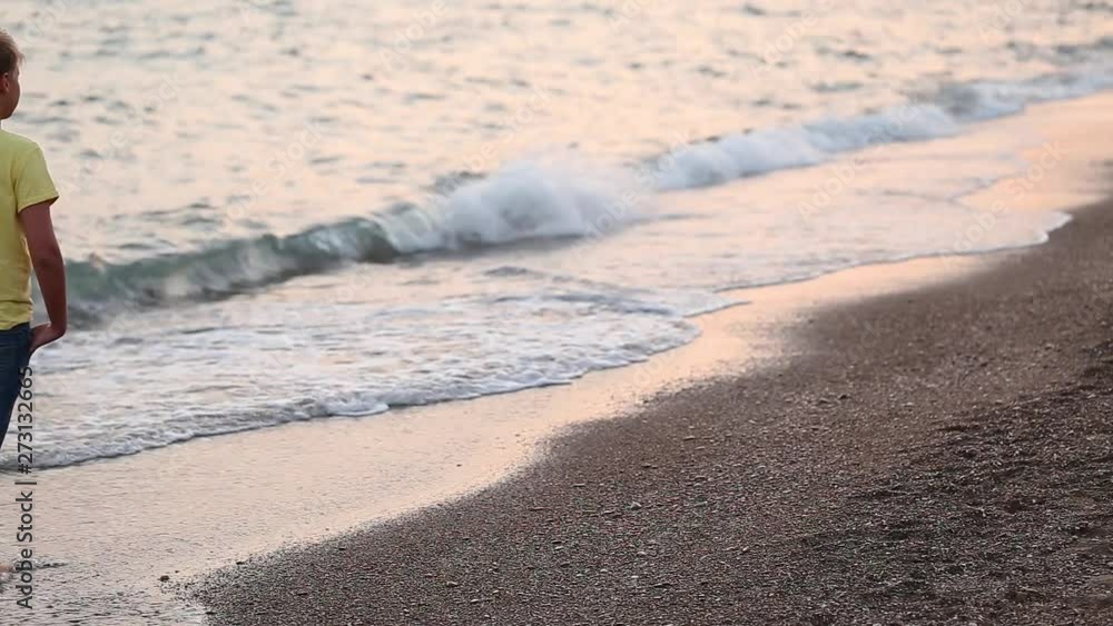 Young kid walking at seashore of resort looking in beautiful wavy sunset golden sea. Real time full hd video footage. Young kid walking at seashore of resort looking in beautiful wavy sunset golden sea. Real time full hd video footage.