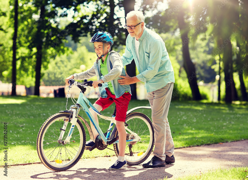 Obraz premium family, generation, safety and people concept - happy grandfather teaching boy how to ride bicycle at summer park