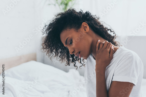 unhappy african american woman suffering from neck pain in bedroom photo