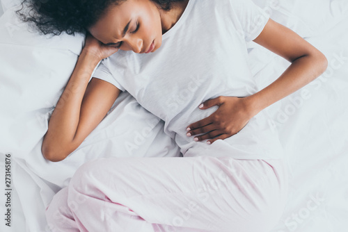 Slika na platnu pretty african american woman suffering from stomach pain while lying in bed