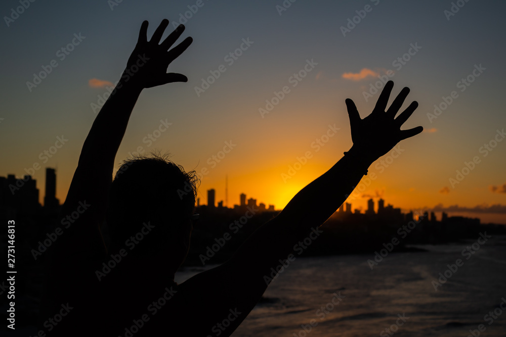 Man facing the sunset sun with his hands outstretched. Sensation of happiness and joy.