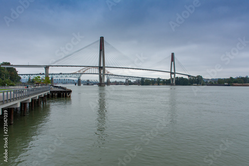 Fototapeta Naklejka Na Ścianę i Meble -  The Patullo bridge in New Westminster, British Columbia, Canada from the Quay looking to the Fraser River and skytrain bridge, Surrey, and blue sky.