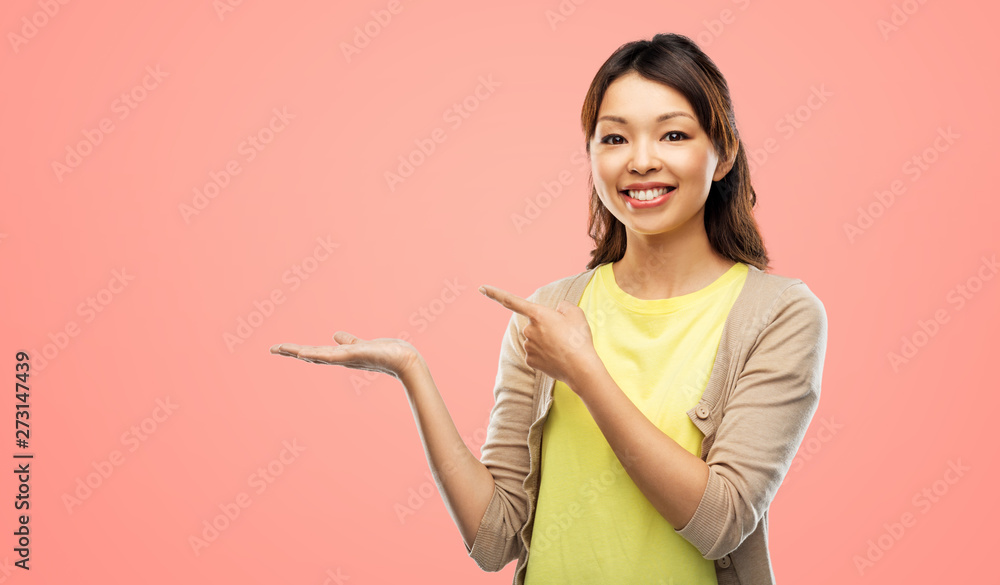people and advertisement concept - happy asian young woman holding something imaginary on empty hand over pink living coral background people and advertisement concept - happy asian young woman holding something imaginary on empty hand over pink living coral background