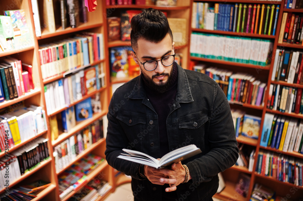 Tall smart arab student man, wear on black jeans jacket and eyeglasses, at library with book at hands. Tall smart arab student man, wear on black jeans jacket and eyeglasses, at library with book at hands.