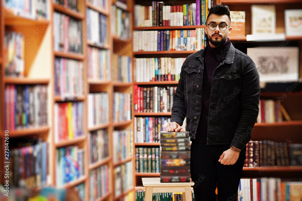 Tall smart arab student man, wear on black jeans jacket and eyeglasses, at library with stack of books. Tall smart arab student man, wear on black jeans jacket and eyeglasses, at library with stack of books.