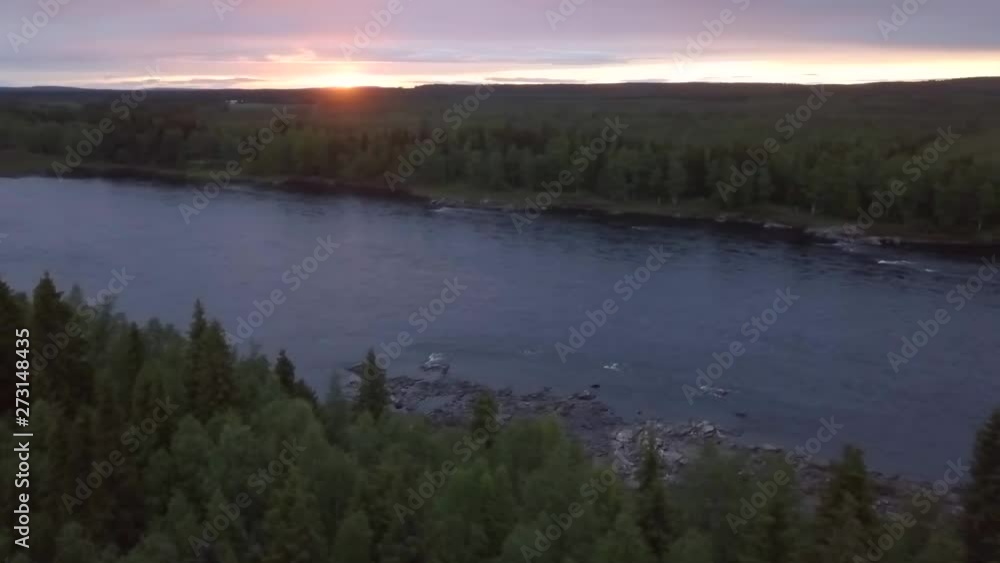 Aerial, pan, drone shot, of the Tornionjoki river, surrounded with spruce forest, at sunset, on nightless night or midnight Sun, in Pello, Lapland, Finland Aerial, pan, drone shot, of the Tornionjoki river, surrounded with spruce forest, at sunset, on nightless night or midnight Sun, in Pello, Lapland, Finland