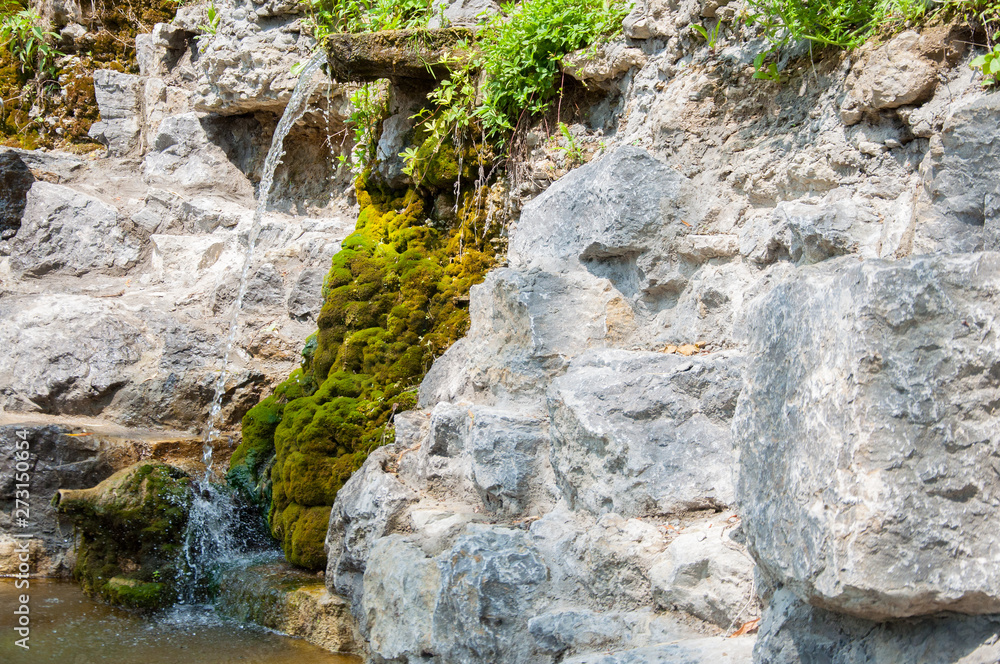 rocky cliff overgrown with green moss. A small waterfall or stream of cold water. Summer rocky cliff overgrown with green moss. A small waterfall or stream of cold water. Summer