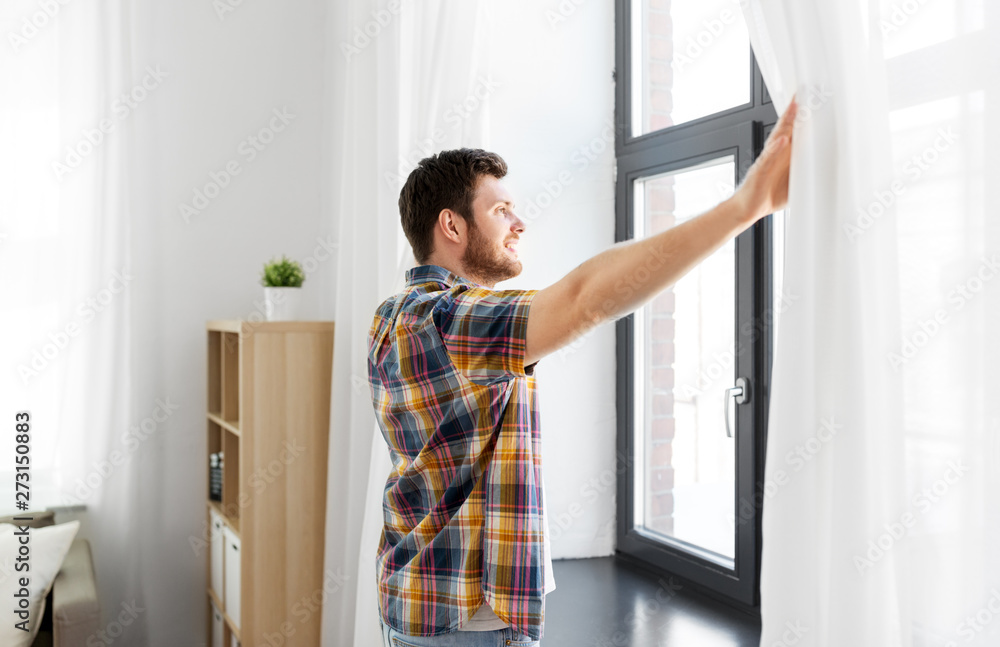 people concept - young man opening window curtain at home people concept - young man opening window curtain at home
