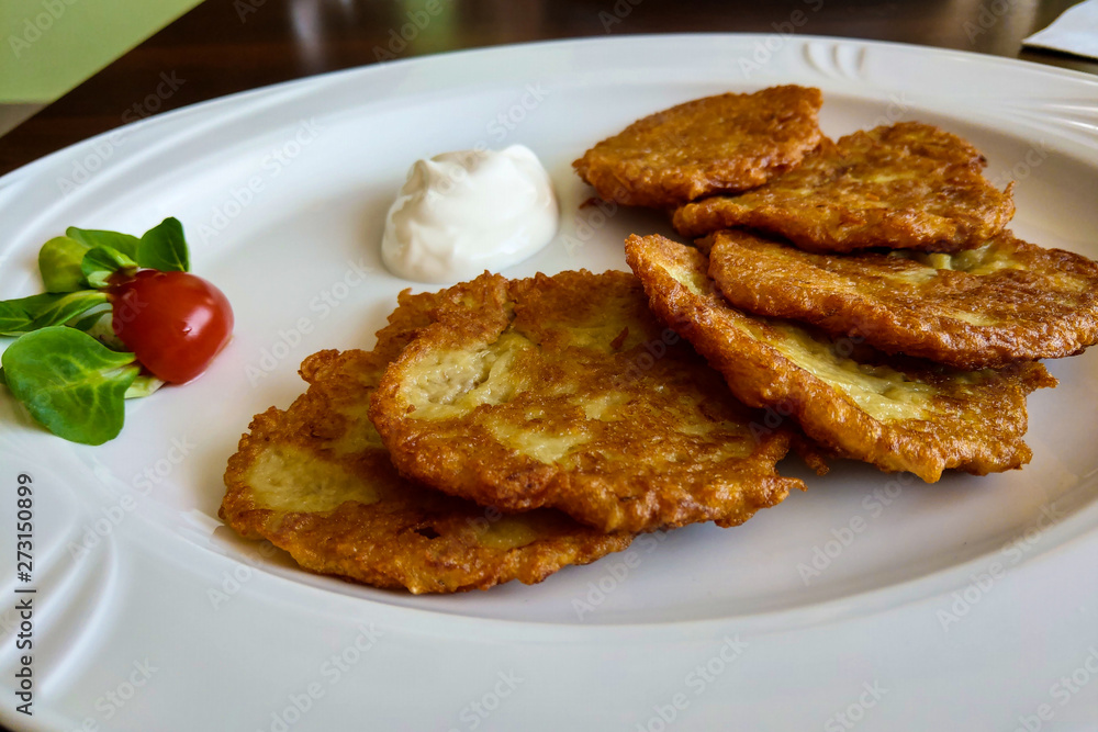 Delicious homemade potato pancakes on plate with sour cream.