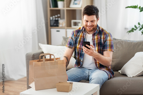 technology, consumption and people concept - smiling man using smartphone for food delivery at home