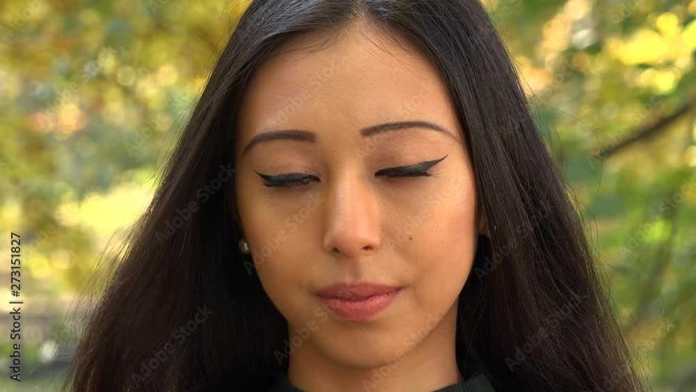 A young Asian woman looks seriously at the camera in a park - face closeup A young Asian woman looks seriously at the camera in a park - face closeup