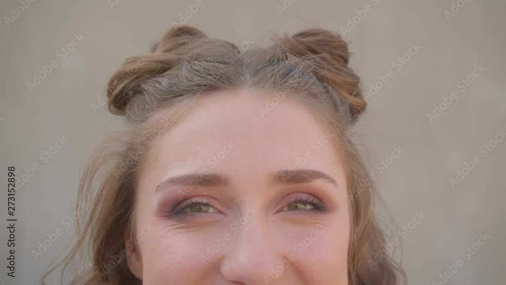 Closeup shoot of young cute caucasian female face with hair buns with eyes looking at camera with urban city on the background Closeup shoot of young cute caucasian female face with hair buns with eyes looking at camera with urban city on the background