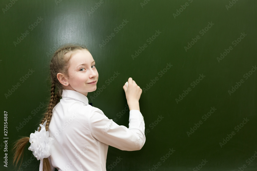 A girl of 10-12 years old is writing on the blackboard. Schoolgirl teen with chalk on a blackboard writes solution to the problem.