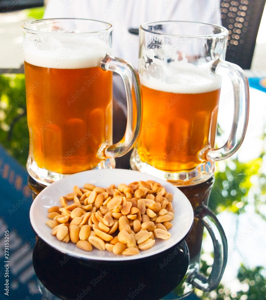 Two glasses of light beer and nuts in the foreground Two glasses of light beer and nuts in the foreground