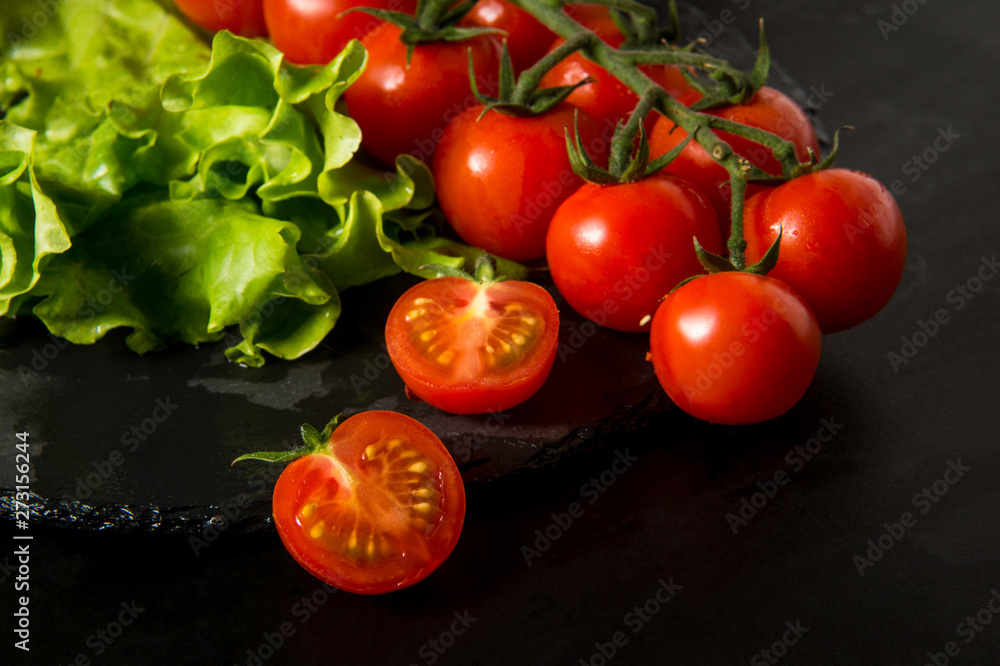 Cherry tomatoes and lettuce lie on a dark surface. Ripe cherry tomatoes. Tomatoes are on the table. Tomato sliced. Halved cherry tomatoes. Cherry tomatoes and lettuce lie on a dark surface. Ripe cherry tomatoes. Tomatoes are on the table. Tomato sliced. Halved cherry tomatoes.