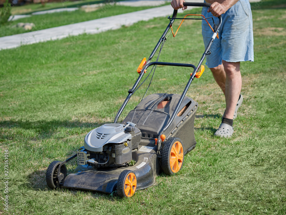 European man is working on the personal plot, he is using lawn mower. European man is working on the personal plot, he is using lawn mower.