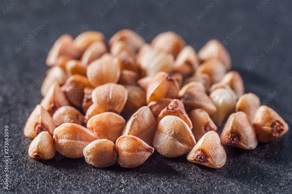 Obraz premium A small pile of buckwheat cereal closeup on a dark background. Macro shooting.