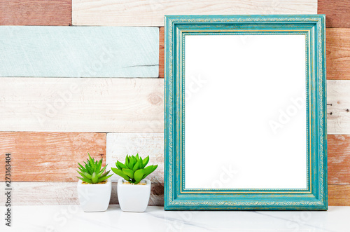 Blank vintage photo frame on wooden wall with cactus plant. © gamjai