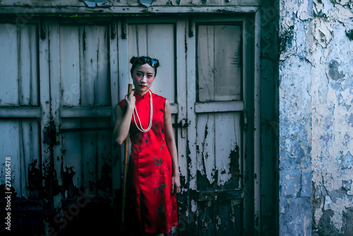 Portrait images of Girl wearing red Cheongsam dress Standing and holding a broom For cleaning with old window and wall background, to instagram concept.