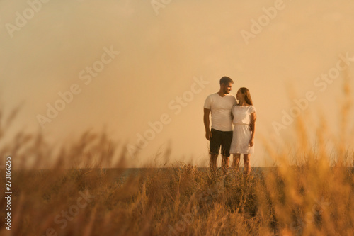man and woman walking in field at sunset