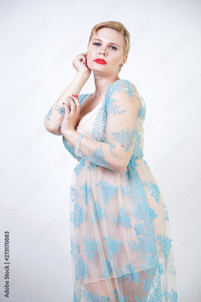 pretty cute blonde woman with short hair and plus size body wearing long  transparent blue lace dress. stylish fashionable adult girl in cute  nightgown on white studio background alone. Stock Photo