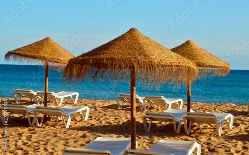 Straw umbrellas with sunbeds at the beach and sea