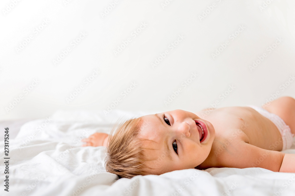 Cute little baby lying on white bed and smiling happily, childhood copy space Cute little baby lying on white bed and smiling happily, childhood copy space