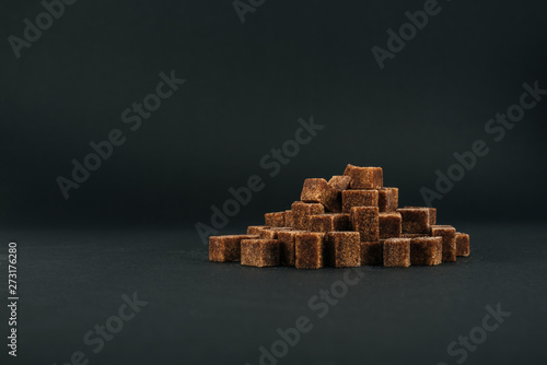 pile of unrefined brown sugar cubes on black background with copy space