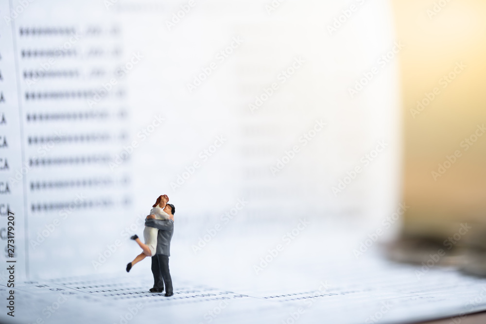 Miniature people: Small couple figures in love standing on bank passbook. Love and Valentine's day concepts. family finance concept. Saving money for get marriage. Miniature people: Small couple figures in love standing on bank passbook. Love and Valentine's day concepts. family finance concept. Saving money for get marriage.