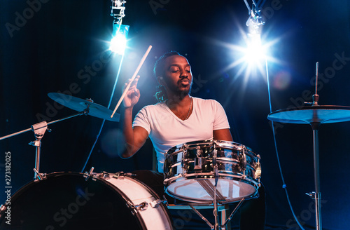 Tablou canvas Young african-american jazz musician or drummer playing drums on blue studio background in glowing smoke around him