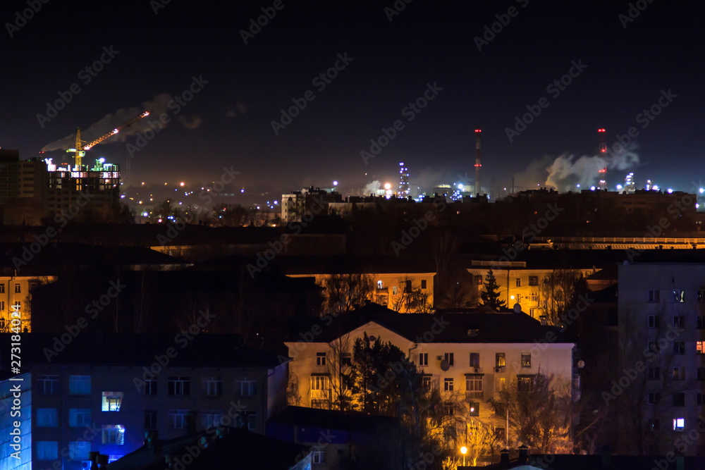 Night shot of the oil refinery on the city skyline. Lots of lights. Industrial and residential areal. Air Pollution and Climate Change.Smoke from the pipes of the factory