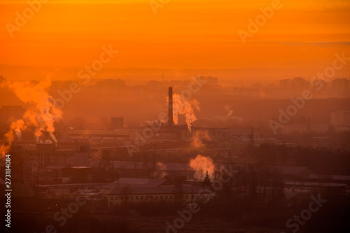 Sunrise over factory at the industrial area. Orange light rays comes through morning fog and smoke from pipes. Industrial chemical manufacturing