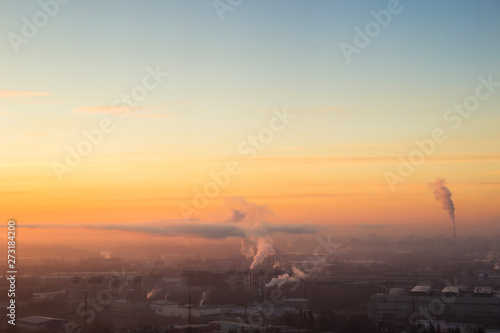 Sunrise over factory at the industrial area. Orange light rays comes through morning fog and smoke from pipes. Power plant