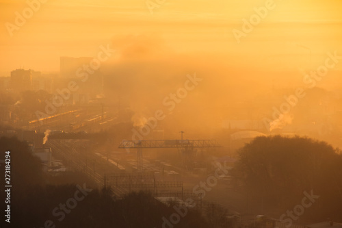 Sunrise over railway at the industrial area. Traffic jam on the bridge. Yellow sun rays comes through morning fog and dust. Containers with goods at the freight depot.Start of busy woking day