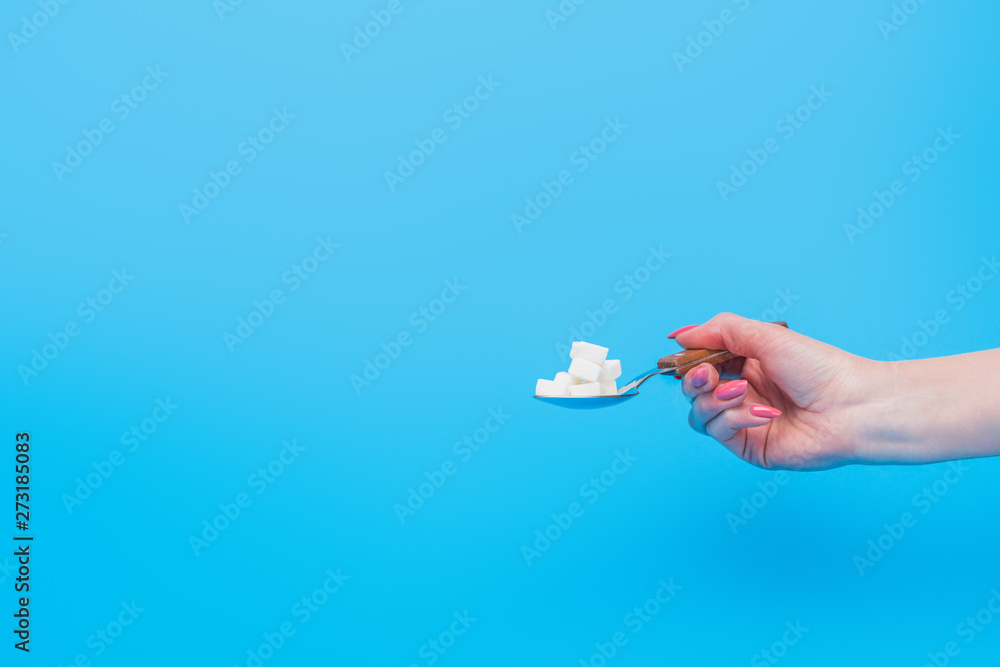 partial view of female hand with teaspoonful of white sugar cubes isolated on blue partial view of female hand with teaspoonful of white sugar cubes isolated on blue