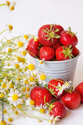 Fototapeta Naklejka Na Ścianę i Meble -  Scattered strawberry berry and in a small bucket on a light background with a bouquet of chamomile flowers . Summer berry season.