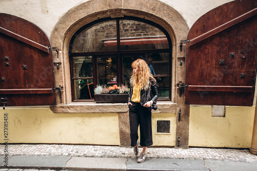 The girl walks with a camera in Prague. A young blonde woman walks along a narrow cobbled street in Prague, Czech Republic. Stylish blonde girl in a leather jacket.