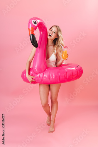 Happy young woman posing isolated over pink wall background dressed in swimwear holding rubber ring beach concept.