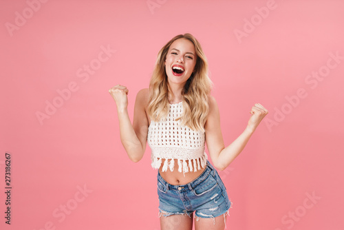 Happy young woman posing isolated over pink wall background make winner gesture.