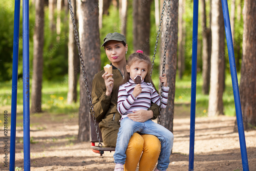 Mother and daughter sitting on teeter-totter, in the park, eating ice cream Mother and daughter sitting on teeter-totter, in the park, eating ice cream