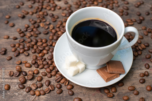 white cup of coffee on a wooden table, chocolate, sugar and coffee beans,